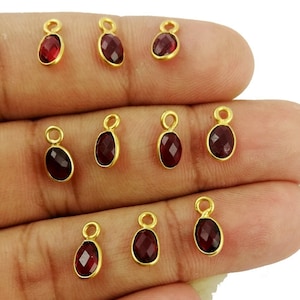 May include: Ten gold-plated oval-shaped charms with red gemstone accents. Each charm has a loop for attaching to jewelry.