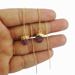 May include: Gold-tone chain earrings with raw, dark pink ruby gemstones. The ruby stones are capped with gold. The earrings have a simple, elegant design, perfect for everyday wear or special occasions.