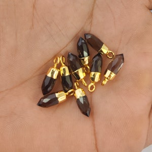 Puede incluir: Un grupo de diez colgantes de piedra preciosa de cuarzo ahumado con tapas y anillos de salto chapados en oro. Los colgantes son facetados y tienen una forma puntiaguda.