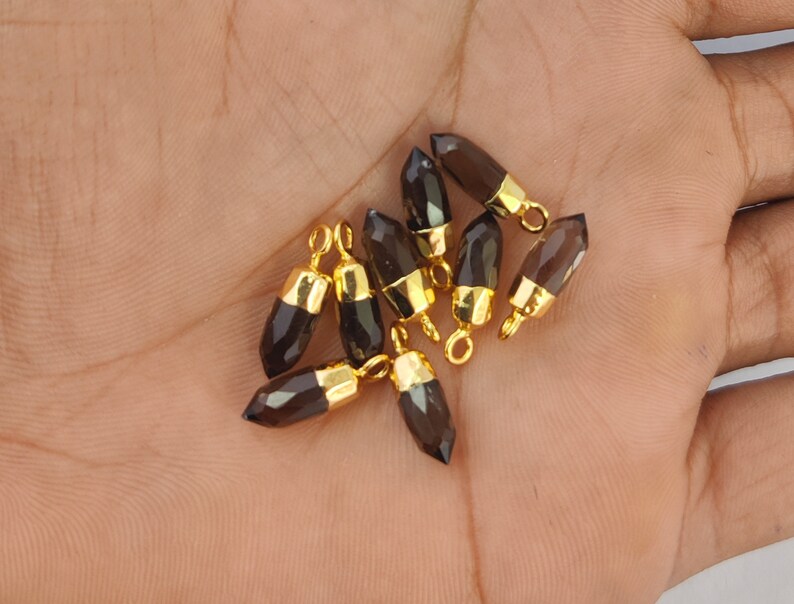 Puede incluir: Un grupo de diez colgantes de piedra preciosa de cuarzo ahumado con tapas y anillos de salto chapados en oro. Los colgantes son facetados y tienen una forma puntiaguda.