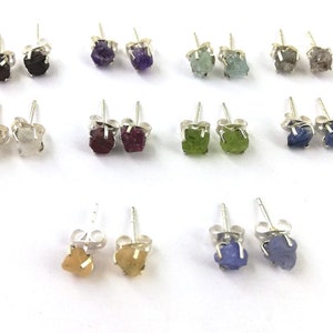 Puede incluir: Un conjunto de 12 pares de pendientes de plata con detalles de piedras preciosas en bruto. Las piedras preciosas son de varios colores, incluyendo azul, verde, morado, rojo y blanco.