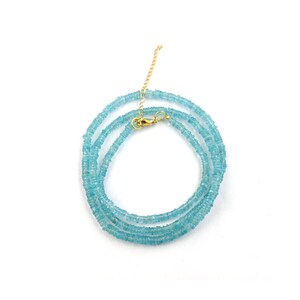 May include: A delicate necklace featuring small, light blue gemstones strung together. The necklace has a gold-colored clasp and chain. The gemstones are a soft, pastel blue color, and the necklace is displayed on a white background.