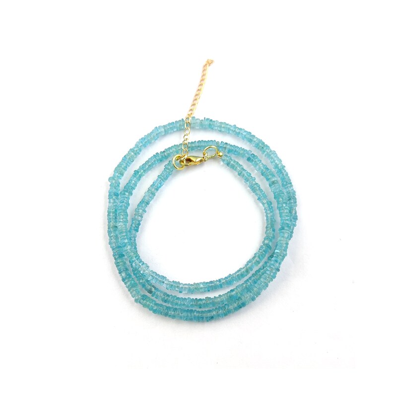May include: A delicate necklace featuring small, light blue gemstones strung together. The necklace has a gold-colored clasp and chain. The gemstones are a soft, pastel blue color, and the necklace is displayed on a white background.
