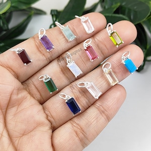 Puede incluir: Surtido de 12 colgantes de piedras preciosas en varios colores, incluyendo amatista, aguamarina, rubí, esmeralda, turquesa, y más. Cada colgante es rectangular y tiene un aro de plata.