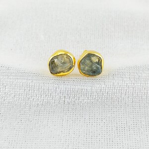 Puede incluir: Un par de pendientes de oro con detalles de piedras preciosas azul claro. Las piedras preciosas tienen una forma irregular y un aspecto &aacute;spero y natural.