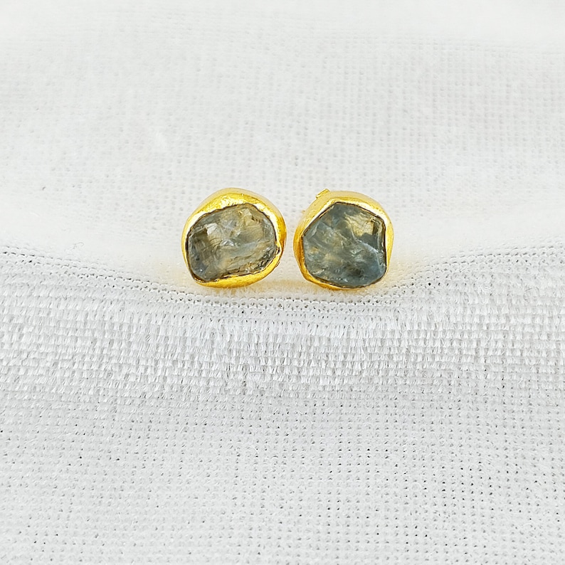 Puede incluir: Un par de pendientes de oro con detalles de piedras preciosas azul claro. Las piedras preciosas tienen una forma irregular y un aspecto &aacute;spero y natural.
