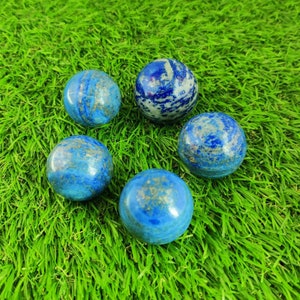 Pu&ograve; includere: Cinque sfere rotonde, lisce, di lapislazzuli blu e oro su uno sfondo di erba artificiale verde.