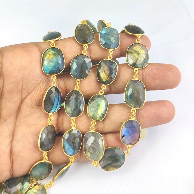 May include: A strand of gold-plated chain with faceted labradorite gemstone beads. The beads are a mix of dark blue, green, and gray with iridescent flashes of color.