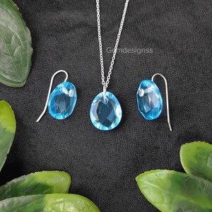 May include: A silver necklace and earrings set with light blue teardrop-shaped crystal pendants.