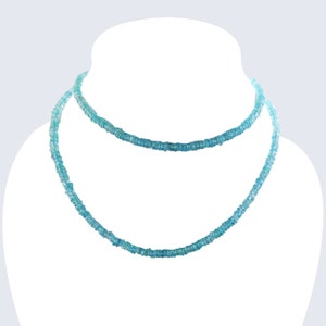 May include: A double-strand necklace displayed on a white mannequin. The necklace is composed of small, light blue beads, creating a delicate and elegant appearance. The beads are evenly spaced, and the necklace has a subtle sparkle.