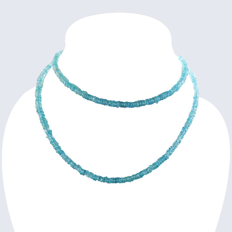 May include: A double-strand necklace displayed on a white mannequin. The necklace is composed of small, light blue beads, creating a delicate and elegant appearance. The beads are evenly spaced, and the necklace has a subtle sparkle.