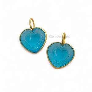 May include: Two heart-shaped pendants with a light blue centre and a gold-coloured frame. The pendants have a loop at the top for hanging. The text "Gemdesignss" is visible on the right side.