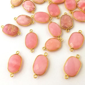 Peut inclure: Une collection de breloques connecteurs ovales en pierre rose avec des accents métalliques dorés. Les breloques ont une finition lisse et polie et sont parfaites pour ajouter une touche d'élégance à vos projets de bijoux.