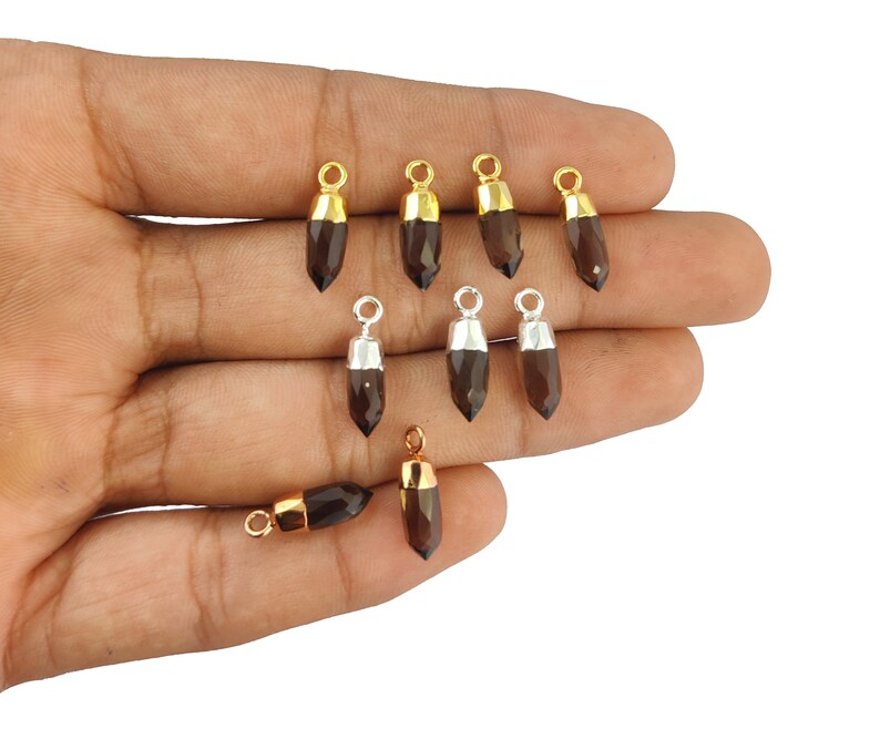Puede incluir: Un conjunto de diez colgantes de piedra preciosa marr&oacute;n con detalles dorados y plateados. Los colgantes tienen forma de l&aacute;grima y una punta puntiaguda. Son perfectos para la elaboraci&oacute;n de joyas.