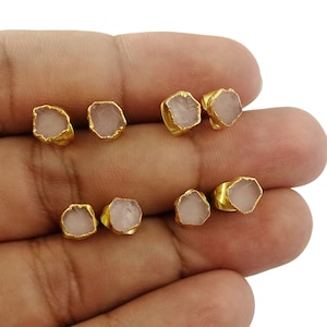May include: Six pairs of gold-plated earrings featuring pink quartz stones. The stones are irregularly shaped and have a natural, raw appearance.