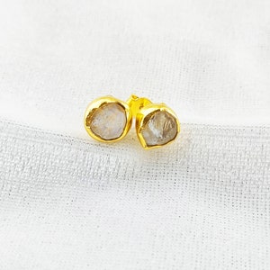 Puede incluir: Un par de pendientes de oro con piedras preciosas transparentes y facetadas. Las piedras tienen una forma irregular y una apariencia ligeramente nublada.