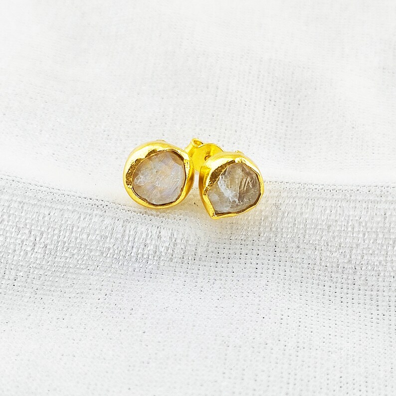 Puede incluir: Un par de pendientes de oro con piedras preciosas transparentes y facetadas. Las piedras tienen una forma irregular y una apariencia ligeramente nublada.