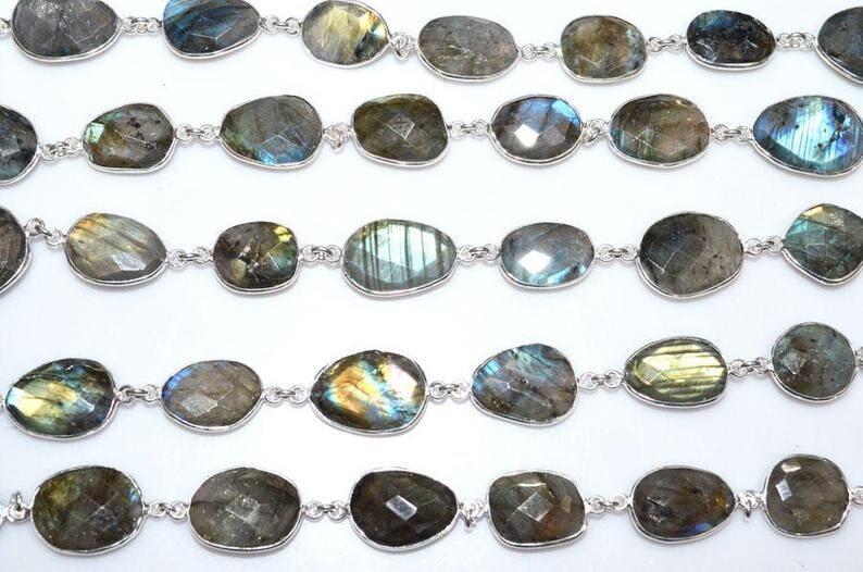 May include: A strand of silver chain with oval-shaped labradorite gemstones. The stones are a mix of green, blue, and gold.