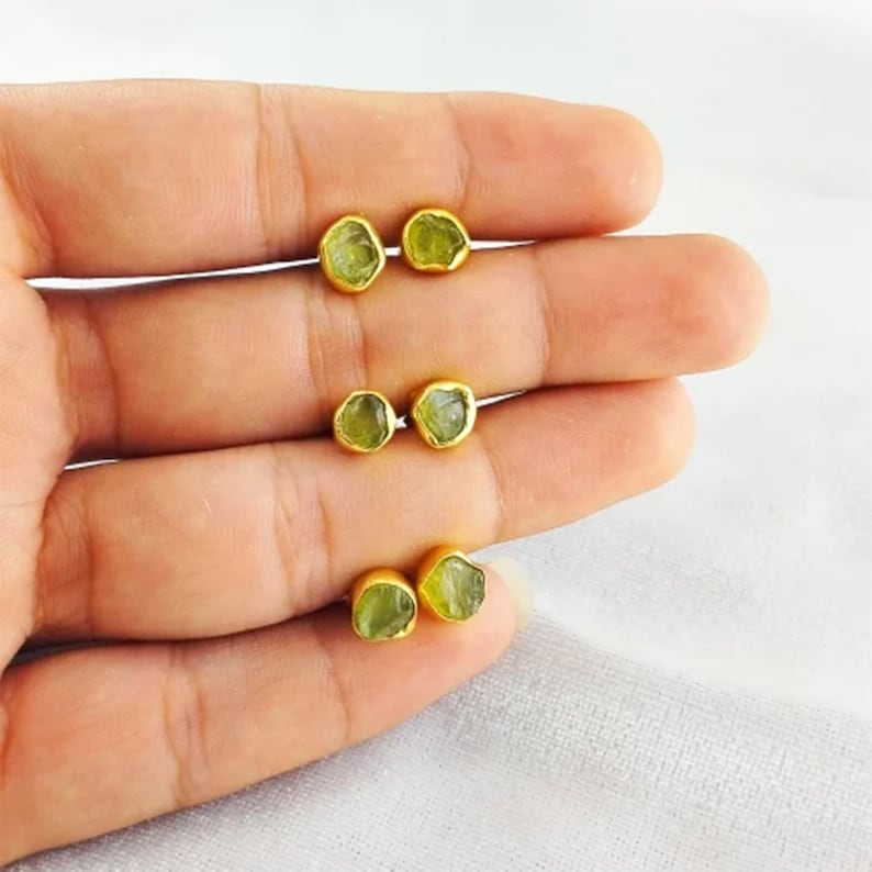 Puede incluir: Un par de pendientes de oro con piedras preciosas verdes. Los pendientes son peque&ntilde;os y delicados, y las piedras preciosas tienen una forma irregular.