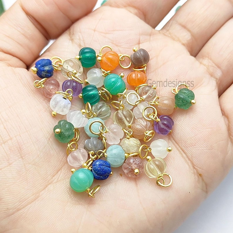 May include: A collection of colorful gemstone beads in various shapes and sizes, including round and pumpkin-shaped designs. The beads are in shades of green, blue, orange, purple, and clear, with gold-colored metal findings. These beads are ideal for jewelry making.
