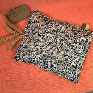 Peut inclure: Un oreiller blanc avec un motif floral dans des tons de vert, bleu et orange. L'oreiller est en tissu et a une couture autour des bords. L'oreiller est sur une surface de couleur corail.