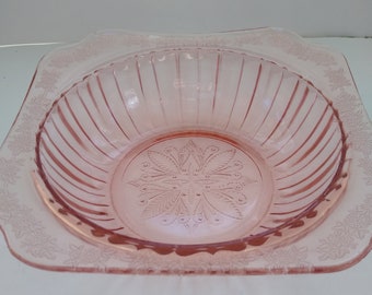 May include: A pink glass bowl with a square rim and a floral design. The bowl has a fluted interior and a raised center design.