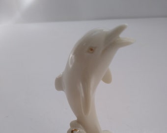 May include: A white porcelain figurine of a dolphin leaping out of the water. The dolphin is painted with gold accents and is standing on a base with a wave design.