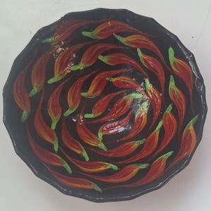 May include: A black, decorative bowl with a spiral design of red and yellow flame-like shapes with green tips. The bowl has a textured rim and a glossy finish, creating a striking contrast.