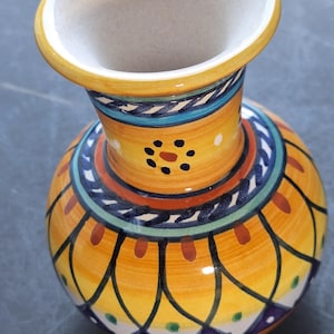 May include: A ceramic vase featuring a vibrant yellow base color with hand-painted decorative patterns in blue, green, orange, and white. The design includes repeating petal-like motifs around the body and a circular floral accent on the neck.