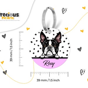 Puede incluir: Una etiqueta redonda para perro, de lunares blancos y negros, con un Boston Terrier blanco y negro asom&aacute;ndose por encima. La etiqueta tiene un fondo rosa con el nombre "Rosy" escrito en blanco.