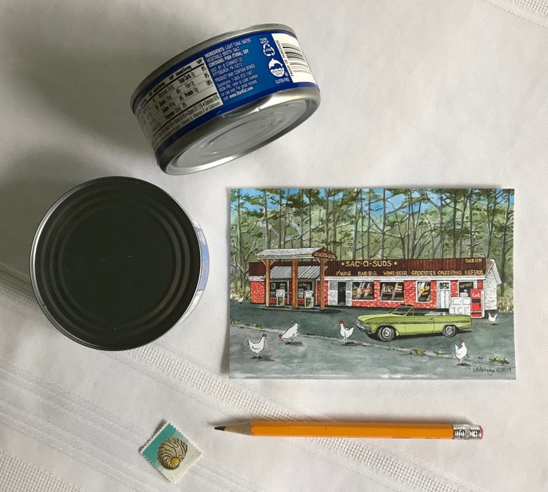 K&ouml;nnte beinhalten: Eine Vintage-Postkarte mit einem gr&uuml;nen Auto, das an einem rot-wei&szlig;en Geb&auml;ude mit dem Text "SAC-O-SUDS" und einem Schild mit der Aufschrift "PIZZA BAR-B-Q WINES GROCERIES & GREETING CARDS" vorbeif&auml;hrt, mit einem Wald im Hintergrund und wei&szlig;en H&uuml;hnern im Vordergrund.