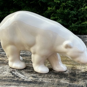 Pode incluir: Uma figura de cerâmica de um urso polar em posição de caminhada. O urso é de cor bege claro com um acabamento brilhante.
