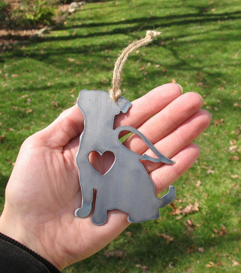 May include: Metal ornament of a dog with wings and a heart cutout. The ornament is silver and has a twine hanger.