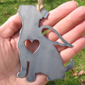 May include: Metal ornament of a dog with a heart cutout and angel wings. The ornament is silver in color and has a rustic finish.