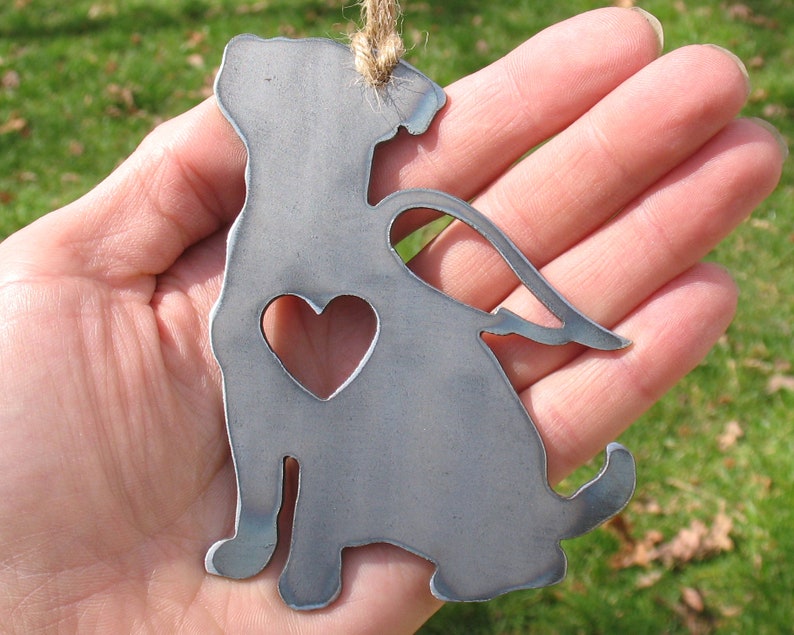 May include: Metal ornament of a dog with a heart cutout and angel wings. The ornament is silver in color and has a rustic finish.