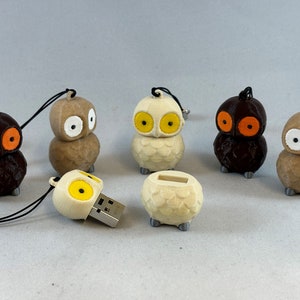 Könnte beinhalten: Sechs USB-Sticks in Form von Eulen mit unterschiedlichfarbigen Augen. Die Eulen sind braun, weiß und beige. Die USB-Sticks sind an Lanyards befestigt.