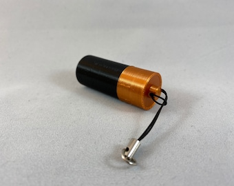 May include: A small black and gold cylindrical container with a black string attached. The container has a gold top and a black bottom.
