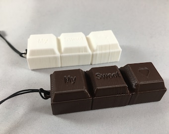 May include: Two chocolate bar keychains, one white and one brown. The white keychain has the words "My Sweet" on it. The brown keychain has the words "My Sweet" and a heart on it.