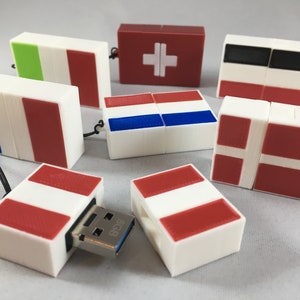 May include: A set of eight USB flash drives, each shaped like a small box with a different country's flag printed on the front. The flags are: France, Italy, Switzerland, Netherlands, Denmark, and Peru. One of the drives is open, revealing a blue USB connector.