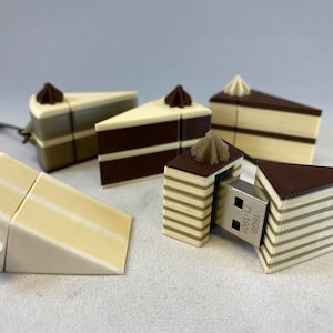 Könnte beinhalten: Ein Satz von fünf USB-Sticks in Kuchenform. Die Sticks sind aus weißem und braunem Kunststoff und haben ein realistisches Kuchendesign. Die Sticks sind alle unterschiedlich groß und geformt, und einige haben ein kleines weißes Frosting-Design auf der Oberseite. Ein Stick ist geöffnet und zeigt einen silbernen USB-Stecker mit dem Text "16GB 71-1601".
