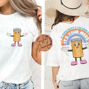 May include: White t-shirt with a cartoon pill bottle graphic and the text "If you're happy & you know it, it's your meds". The pill bottle is smiling and has arms and legs. The text is in a rainbow arc with flowers.
