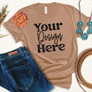 Op de afbeelding: Een bruin T-shirt met de tekst "Your Design Here" in zwart, gecombineerd met een blauwe jeans, een turquoise ketting en een touw. Het shirt heeft een "Instant Download" afbeelding. Een casual, western-thema kledingpresentatie.