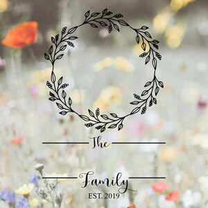 Peut inclure: Une couronne florale noire avec le texte "The Family EST. 2019" sur un fond flou de fleurs color&eacute;es.