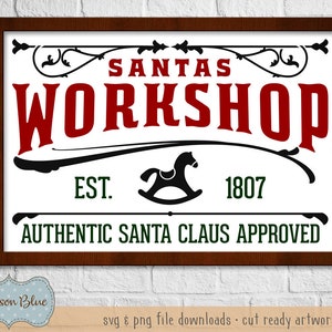 May include: A brown wooden framed sign with white background and black lettering. The sign reads "Santas Workshop Est. 1807 Authentic Santa Claus Approved".