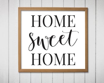 以下が含まれることがあります： 白い背景に黒い文字で「HOME sweet HOME」と書かれた額装されたプリント。フレームは茶色の木です。