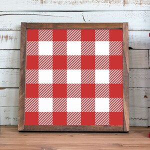 May include: A red and white buffalo check pattern framed in a dark wood frame. The frame is sitting on a wooden surface.
