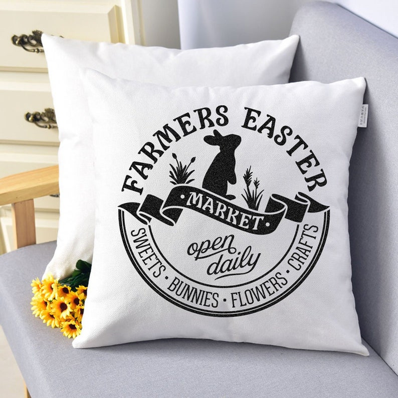 May include: White pillow with black text that reads "Farmers Easter Market open daily Sweets Bunnies Flowers Crafts" with a black silhouette of a rabbit and a banner that reads "Market" in a circle.