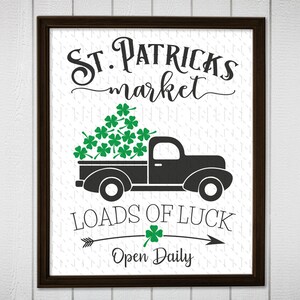 Pode incluir: Um sinal imprimível preto e verde com uma caminhonete preta carregando uma caçamba cheia de trevos verdes. O sinal diz "St. Patricks market" e "Loads of Luck" com um trevo verde e uma seta apontando para a direita. O sinal também diz "Open Daily".