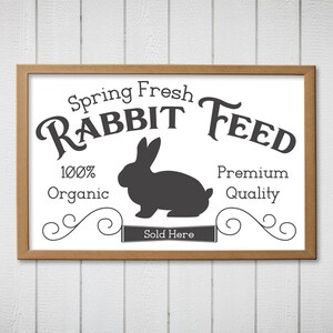 May include: A brown framed sign with white text that reads "Spring Fresh Rabbit Feed 100% Organic Premium Quality Sold Here". A black silhouette of a rabbit is in the center of the sign.