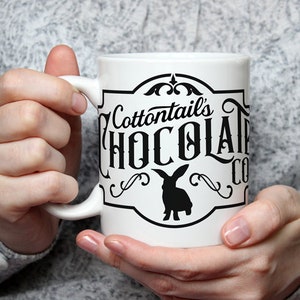 May include: White ceramic mug with a black and white logo that says "Cottontails' Chocolate Co." and features a silhouette of a rabbit.